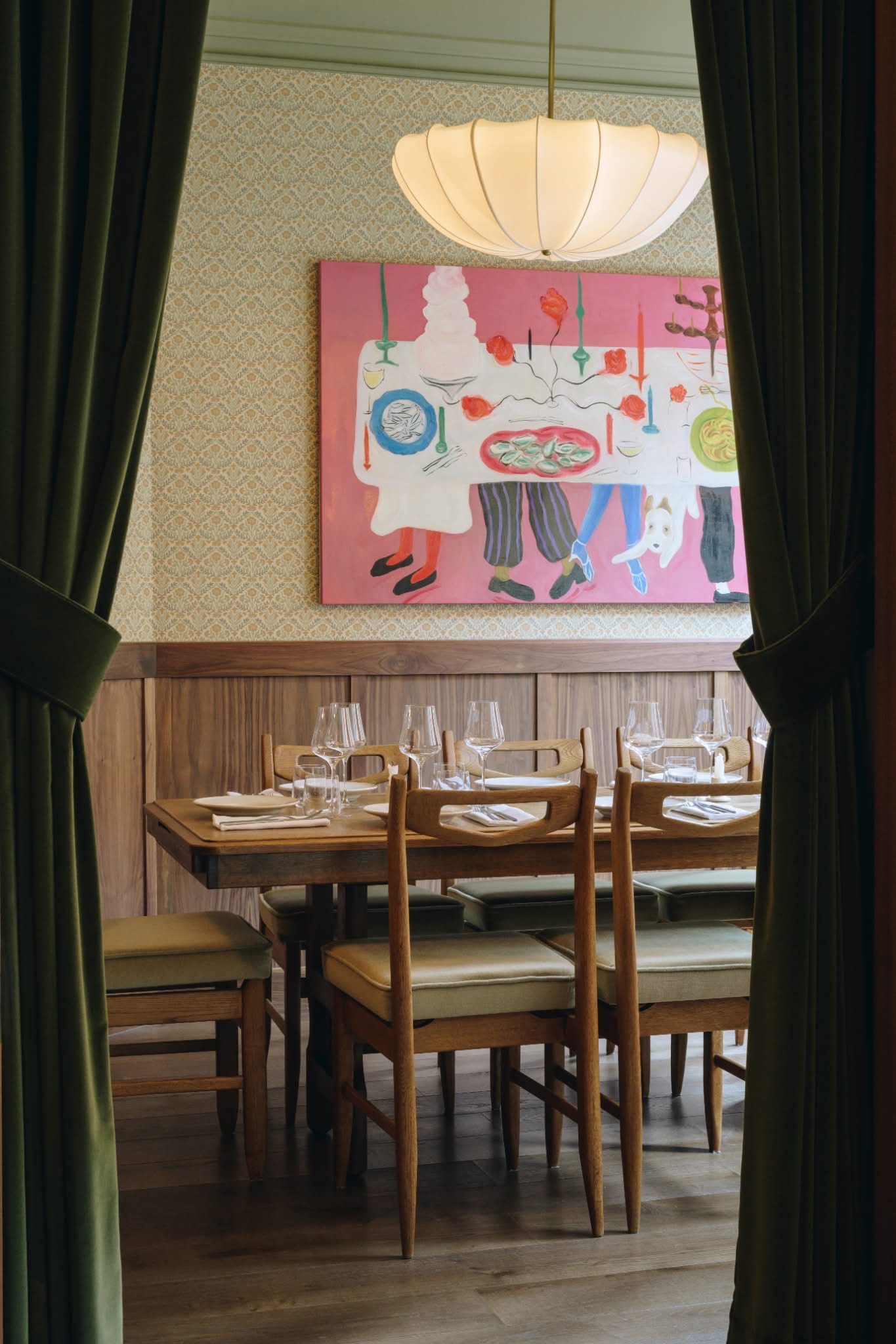 An inventively designed modern bistro features wooden surfaces elevated by sumptuous velvet details, sculptural pendant lighting, and artworks.