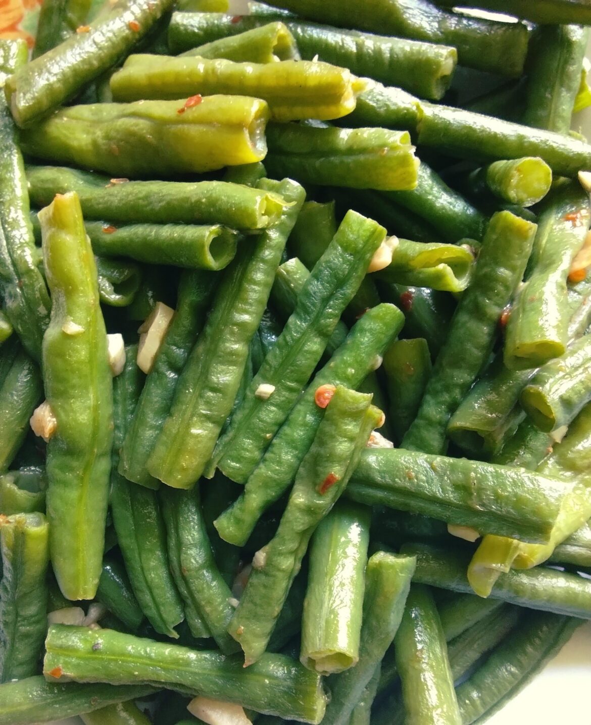 Spicy fried green beans in chili sauce, with black and white pepper, chili flakes and sliced garlic