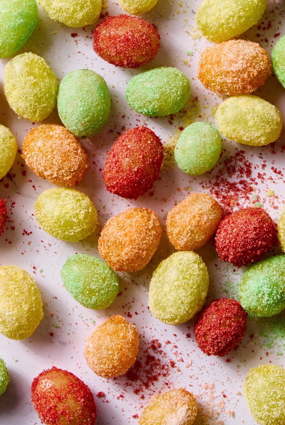 red, yellow, and green colored sour patch green grapes on a light pink background