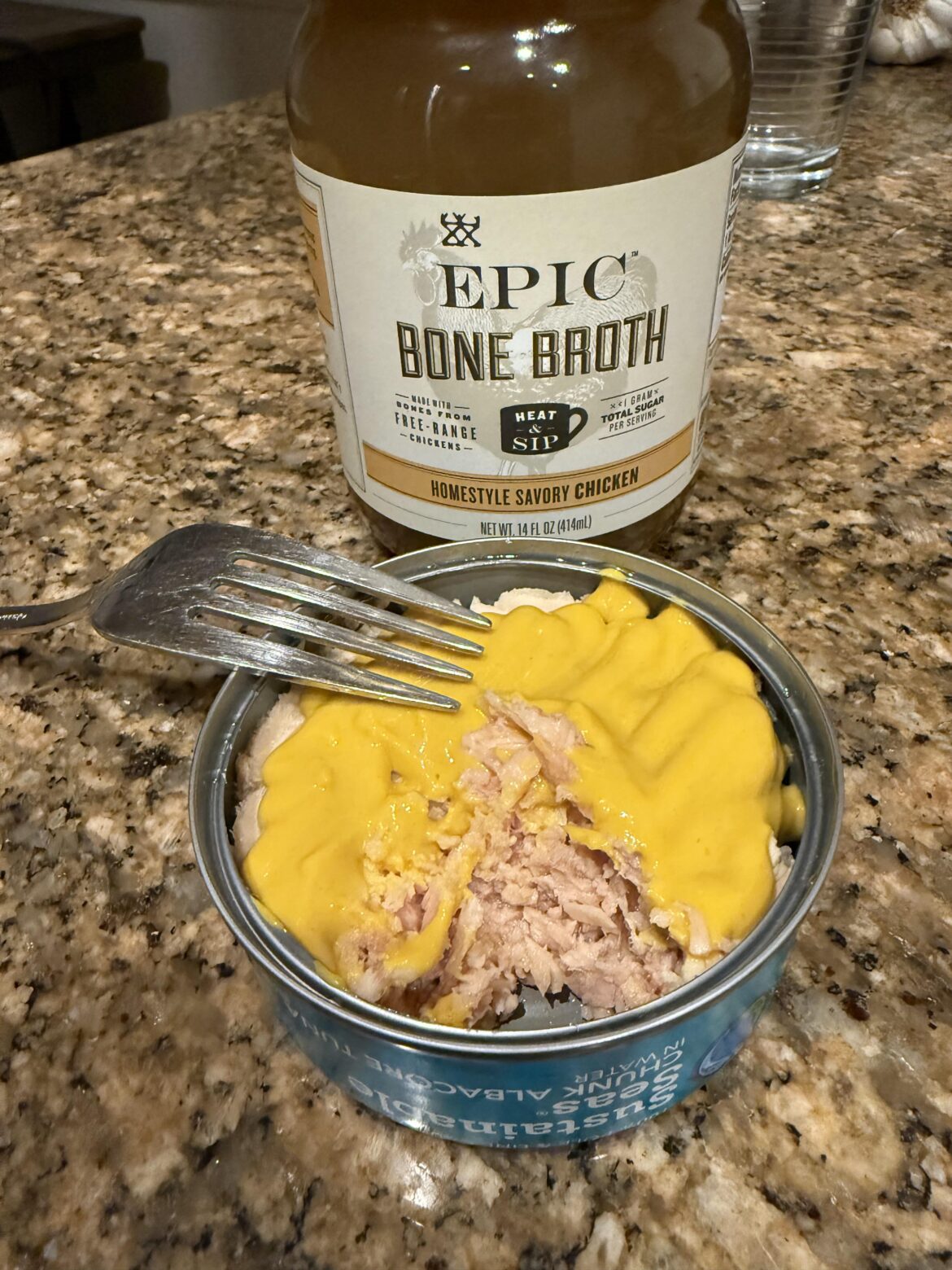 Tuna can layered in yellow mustard, with bone broth to wash it down