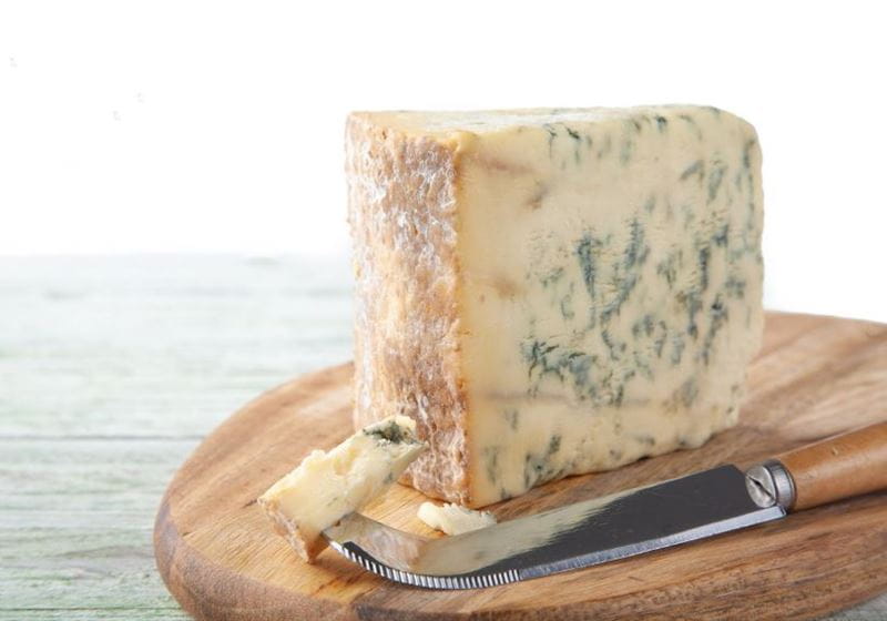 A lump of stilton cheese on a wooden board with a knife by the side