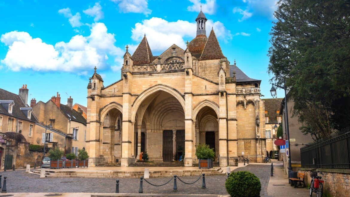 Savor the Best of Beaune: What to Do in France’s Wine Capital A photograph capturing Notre Dame de Beaune in France. The image showcases the exterior of the cathedral, known for its Gothic architecture. The building features characteristic elements such as pointed arches and intricate detailing. Surrounding the cathedral is the urban environment of Beaune, with glimpses of nearby structures.
