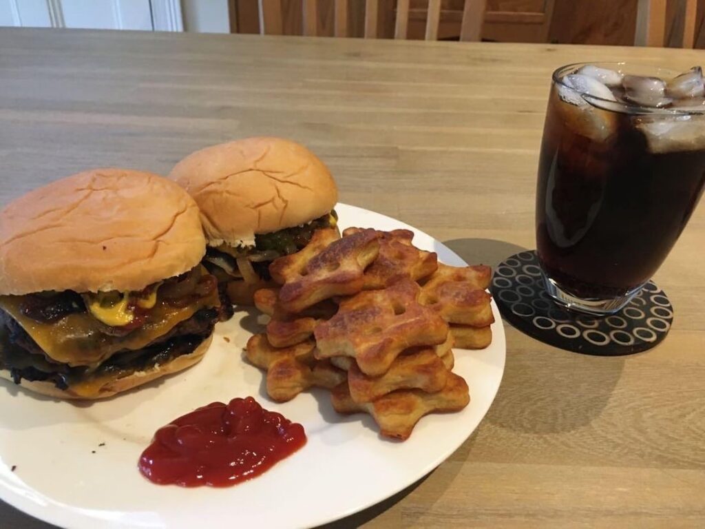 Double cheeseburgers with ketchup, mustard and grilled onions on potato buns, with smiley potato stars and Coke on the side, made by yours truly.
