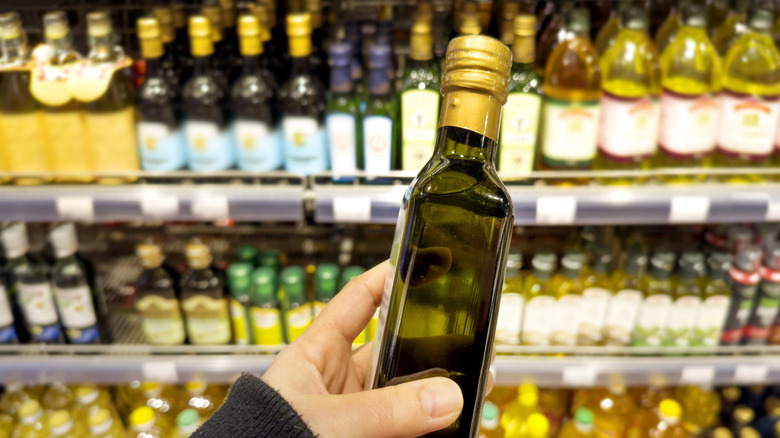 hand holding a small dark bottle of olive oil in oil aisle of grocery store