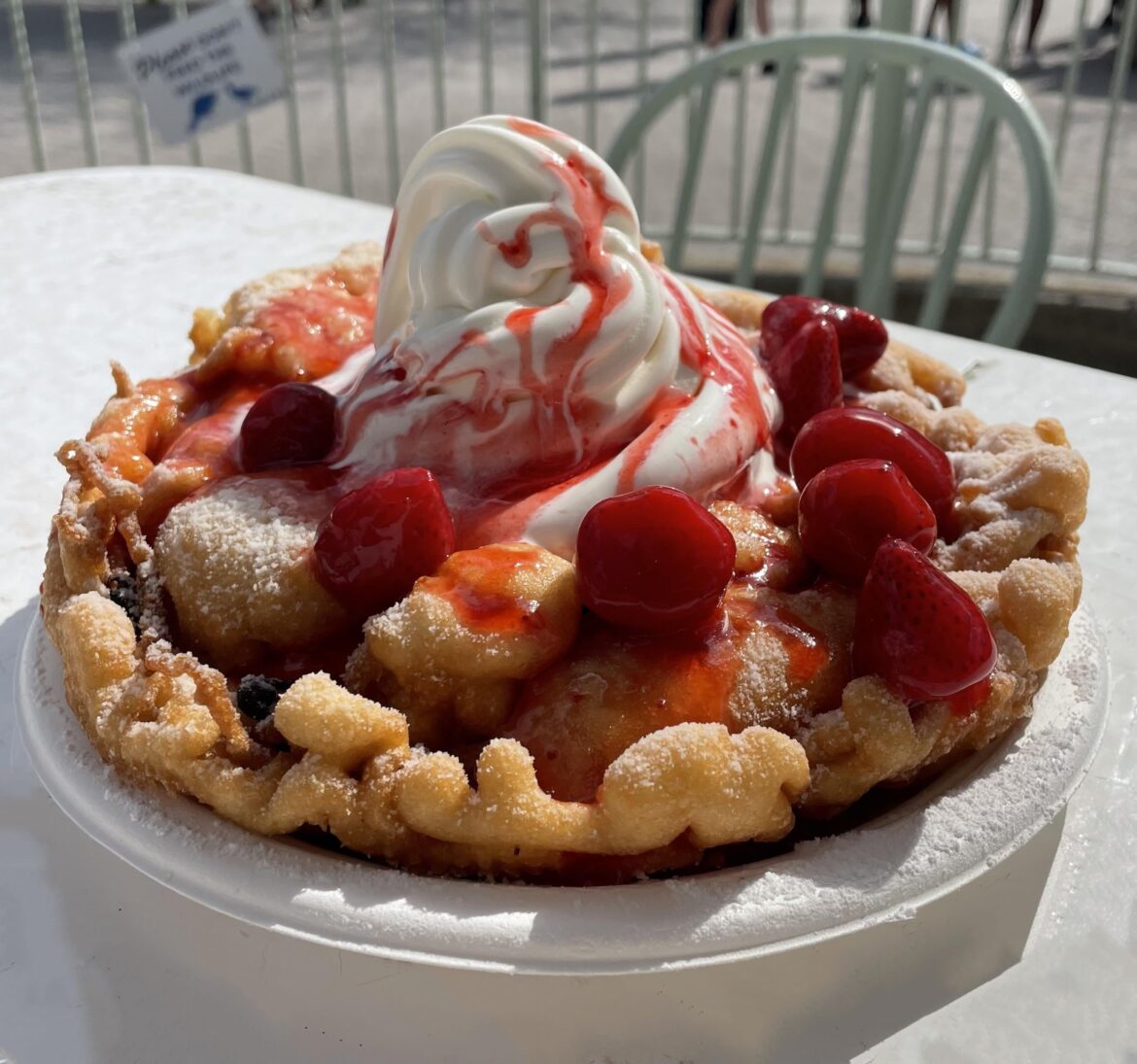 Funnel cake topped with strawberries, strawberry syrup, and vanilla soft-serve.