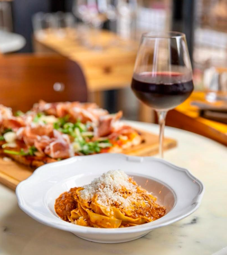A bowl of tagliatelle alla bolognese with grated parmesan cheese on top with a glass of red wine from Yeppa & Co. in Atlanta. 