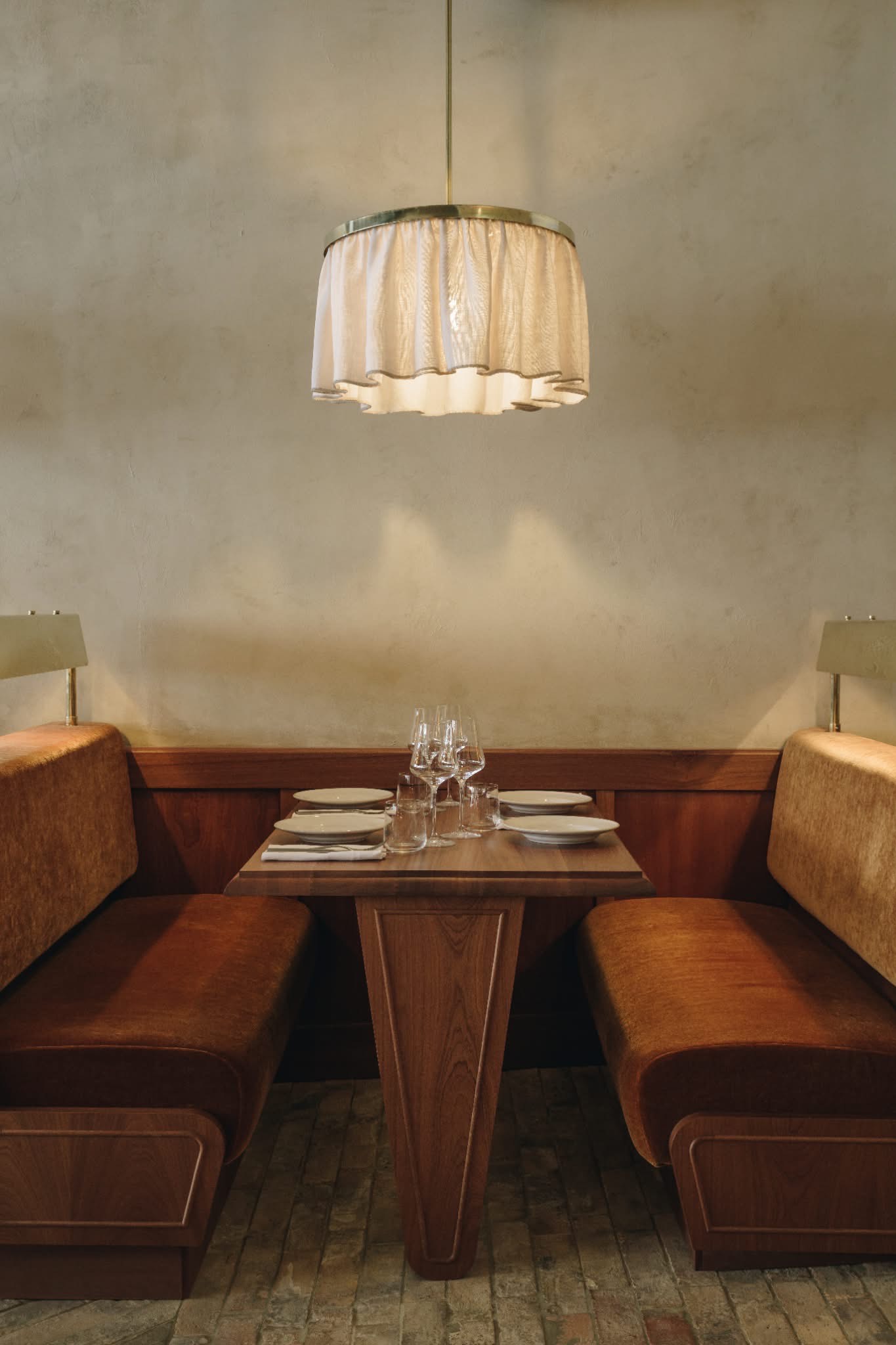 An inventively designed modern bistro features wooden surfaces elevated by sumptuous velvet details, sculptural pendant lighting, and artworks.