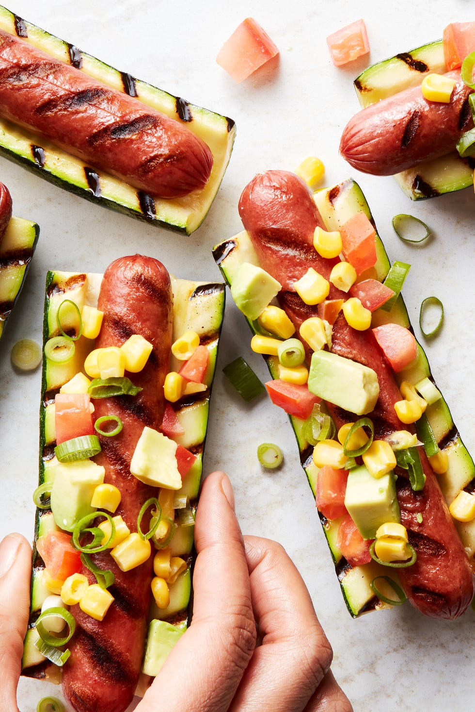 grilled hot dogs in between grilled zucchini topped with avocado salsa