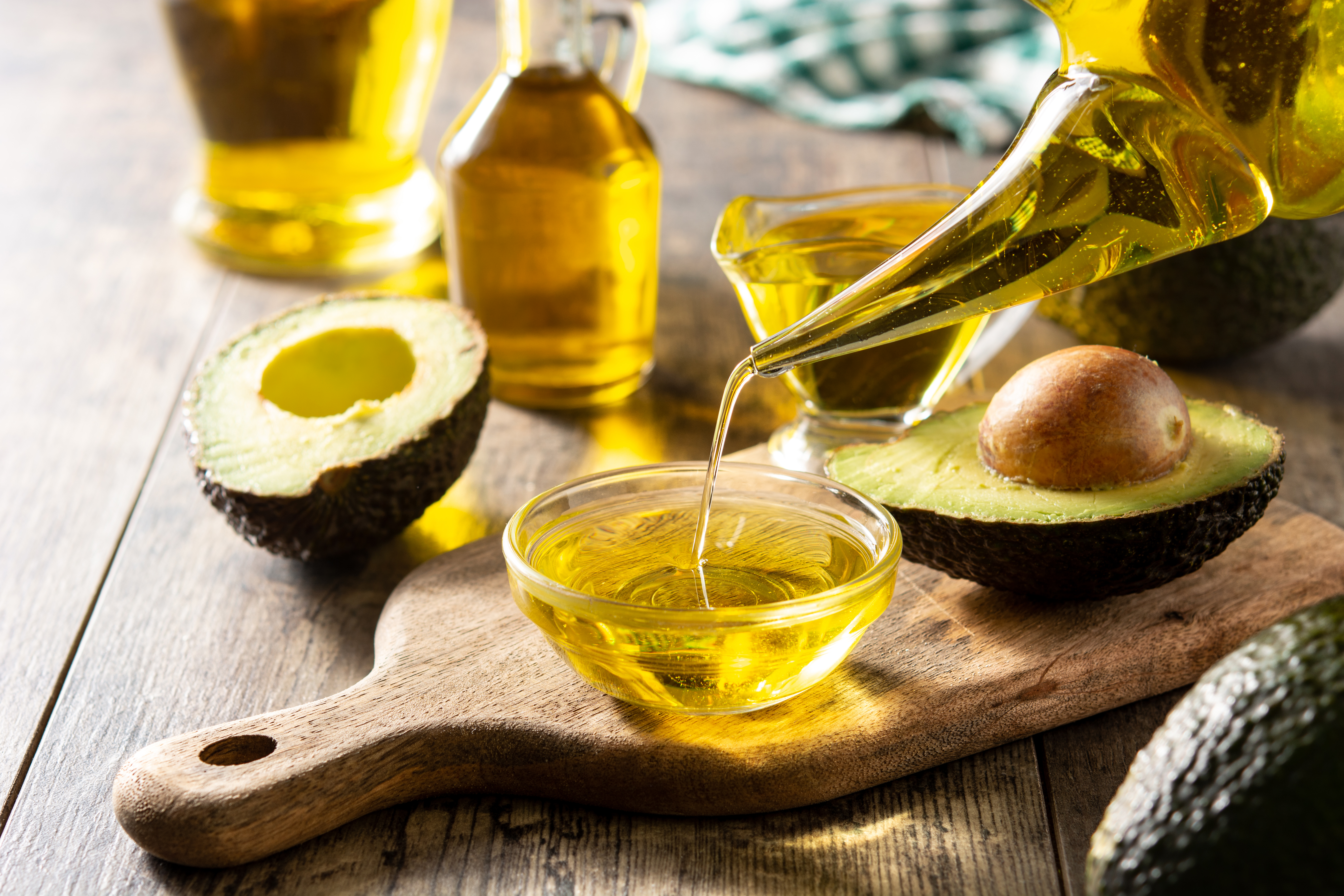 Avocado oil being poured into a bowl next to avocado halves.