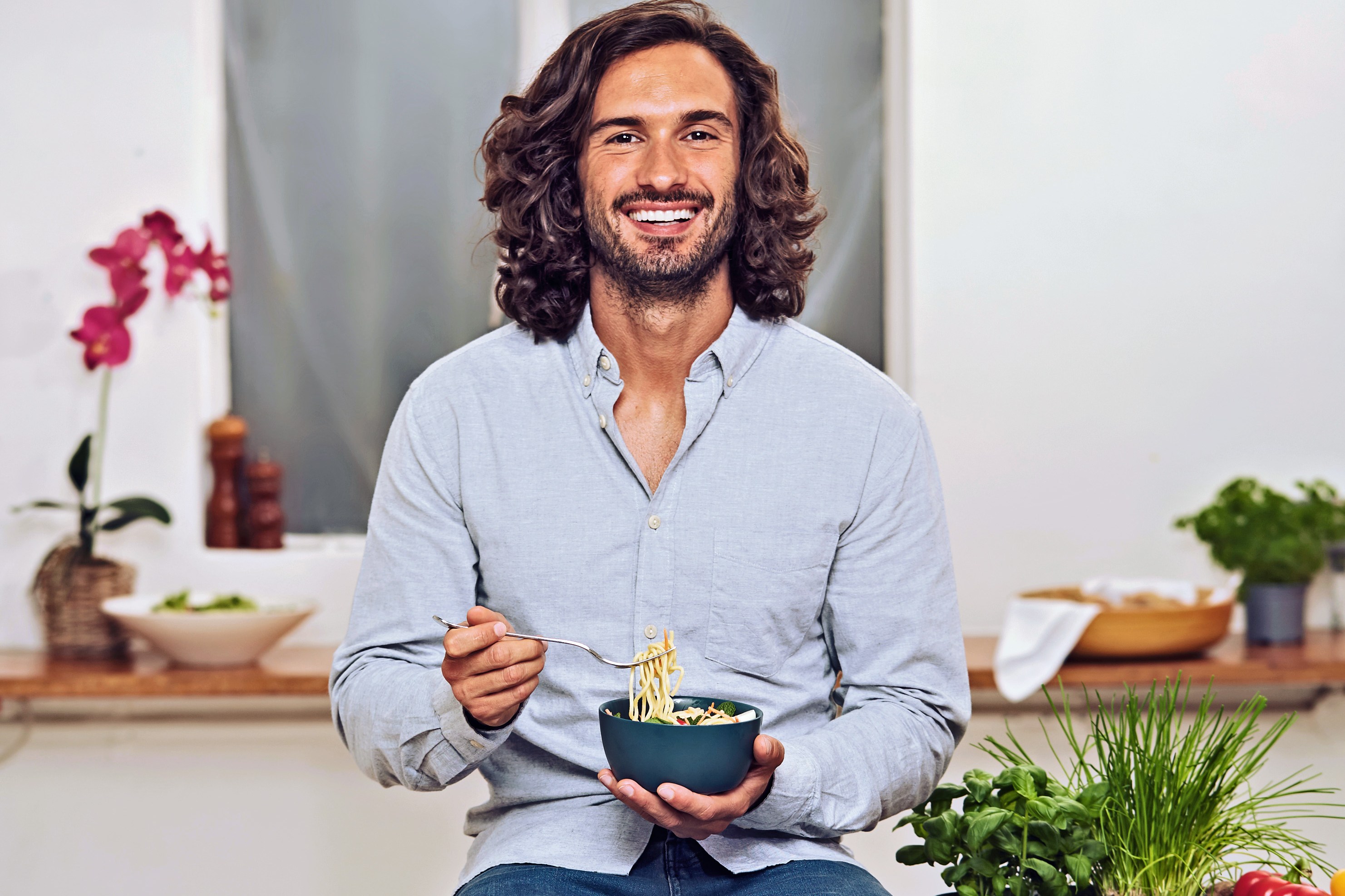 Man sitting on a table, eating a bowl of noodles.
