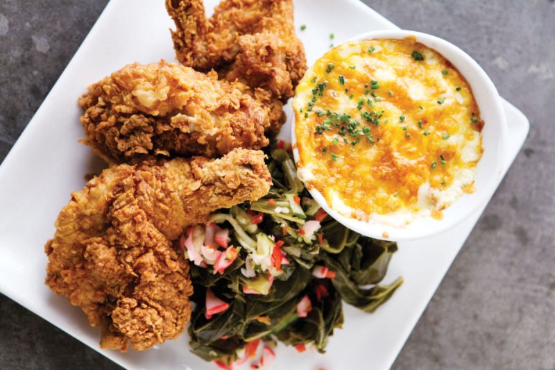Fried chicken on a plate next to some greens and a dipping sauce