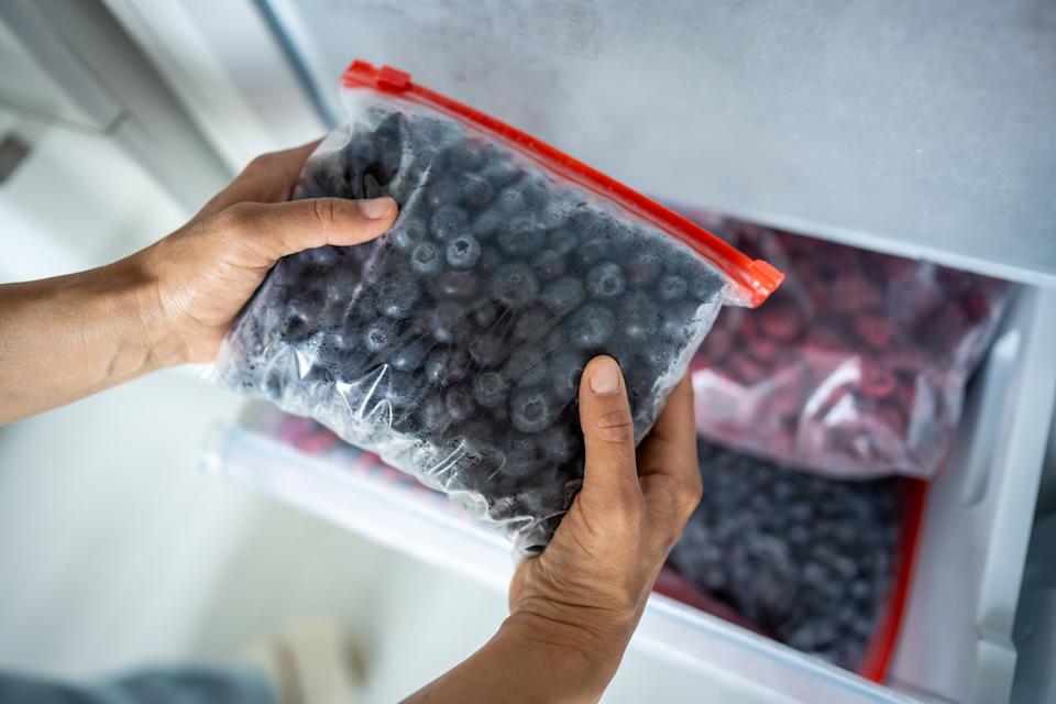 Woman hands hold zip bag with blueberries, putting into freezer. Cost effective food storage, summer berry preservation for winter, vitamins for cold season, quick freezing, nutritional benefits