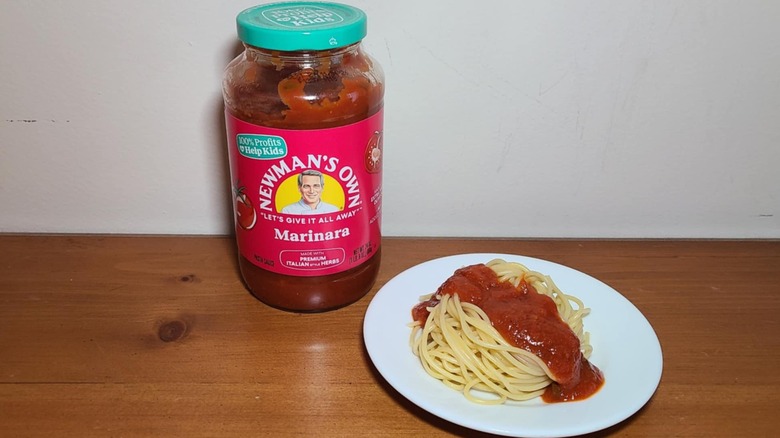 Jar of Newman's Own pasta sauce with a small white plate of spaghetti topped with sauce
