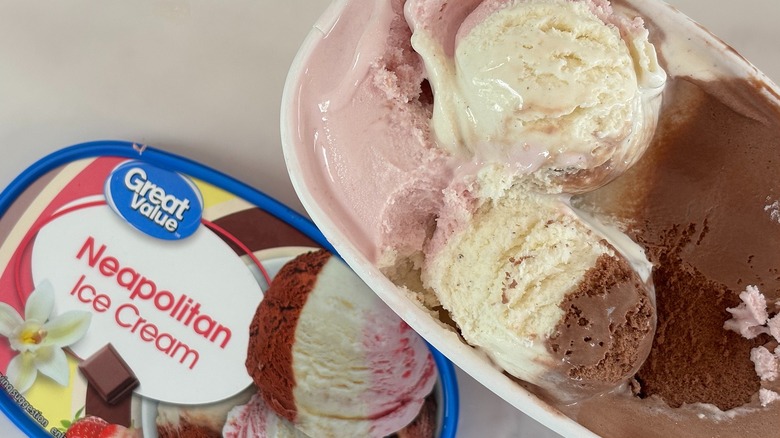 Top-down view of open tub of Great Value Neapolitan ice cream next to lid on white table