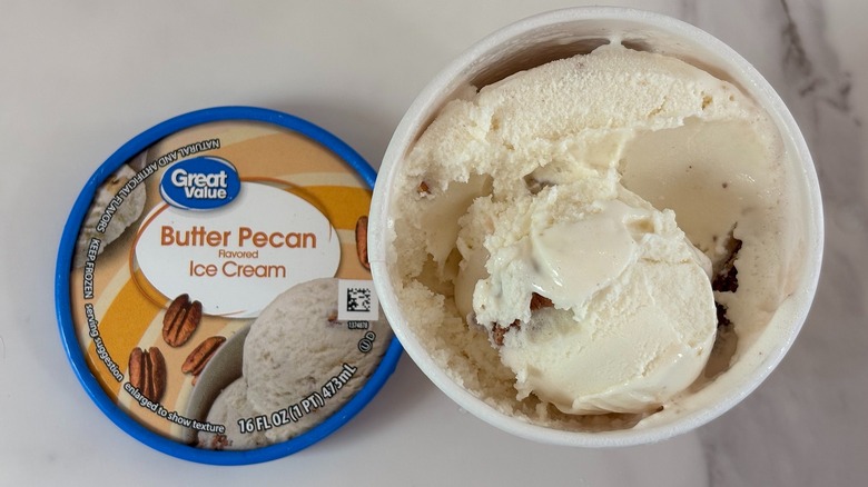 Top-down view of open tub of Great Value Butter Pecan ice cream next to lid on white table