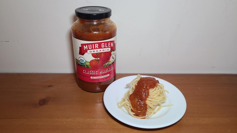 Jar of Muir Glen pasta sauce with a small white plate of spaghetti topped with sauce