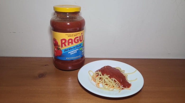 Jar of Ragú pasta sauce with a small white plate of spaghetti topped with sauce