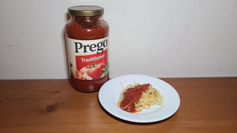 Jar of Prego pasta sauce with a small white plate of spaghetti topped with sauce