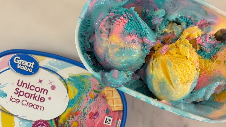 Top-down view of open tub of Great Value Unicorn Sparkle ice cream next to lid on white table
