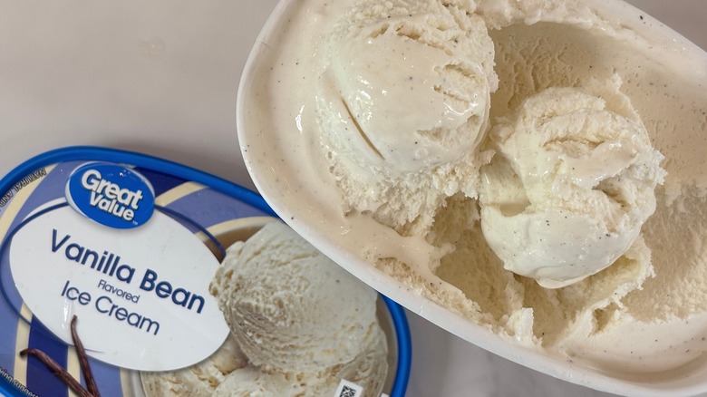 Top-down view of open tub of Great Value Vanilla Bean ice cream next to lid on white table
