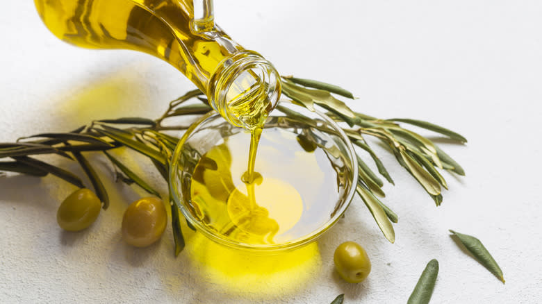 Olive oil poured into a glass near olives and an olive branch