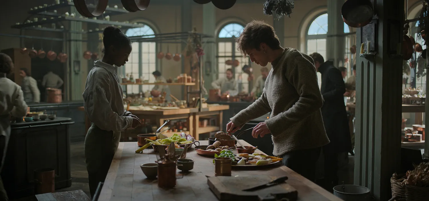 A woman and a man stand on opposite sides of a table as they prepare food.