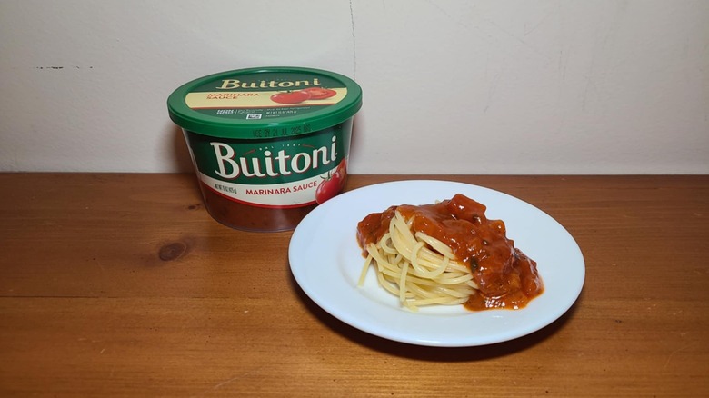 Container of Buitoni pasta sauce with a small white plate of spaghetti topped with sauce