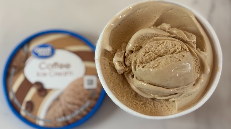 Top-down view of open tub of Great Value Coffee ice cream next to lid on white table
