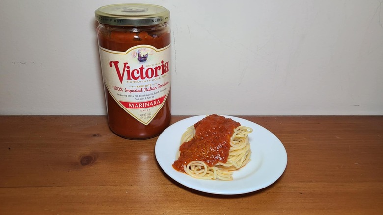 Jar of Victoria pasta sauce with a small white plate of spaghetti topped with sauce