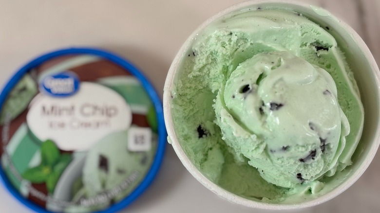 Top-down view of open tub of Great Value Mint Chip ice cream next to lid on white table
