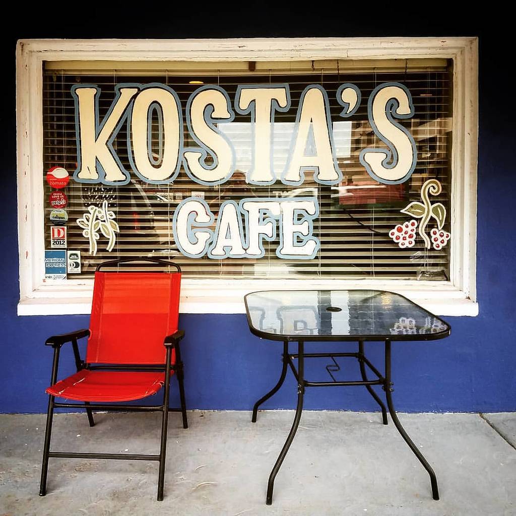 Image shows exterior of Kosta's Cafe in Dallas with a chair and table placed on the front patio.