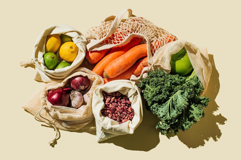 Variety Fresh of organic fruits and vegetables and healthy vegan meal ingredients in reusable eco cotton bags on beige background