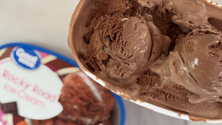 Top-down view of open tub of Great Value Rocky Road ice cream next to lid on white table