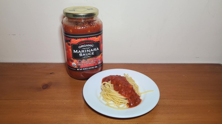 Jar of Trader Joe's pasta sauce with a small white plate of spaghetti topped with sauce