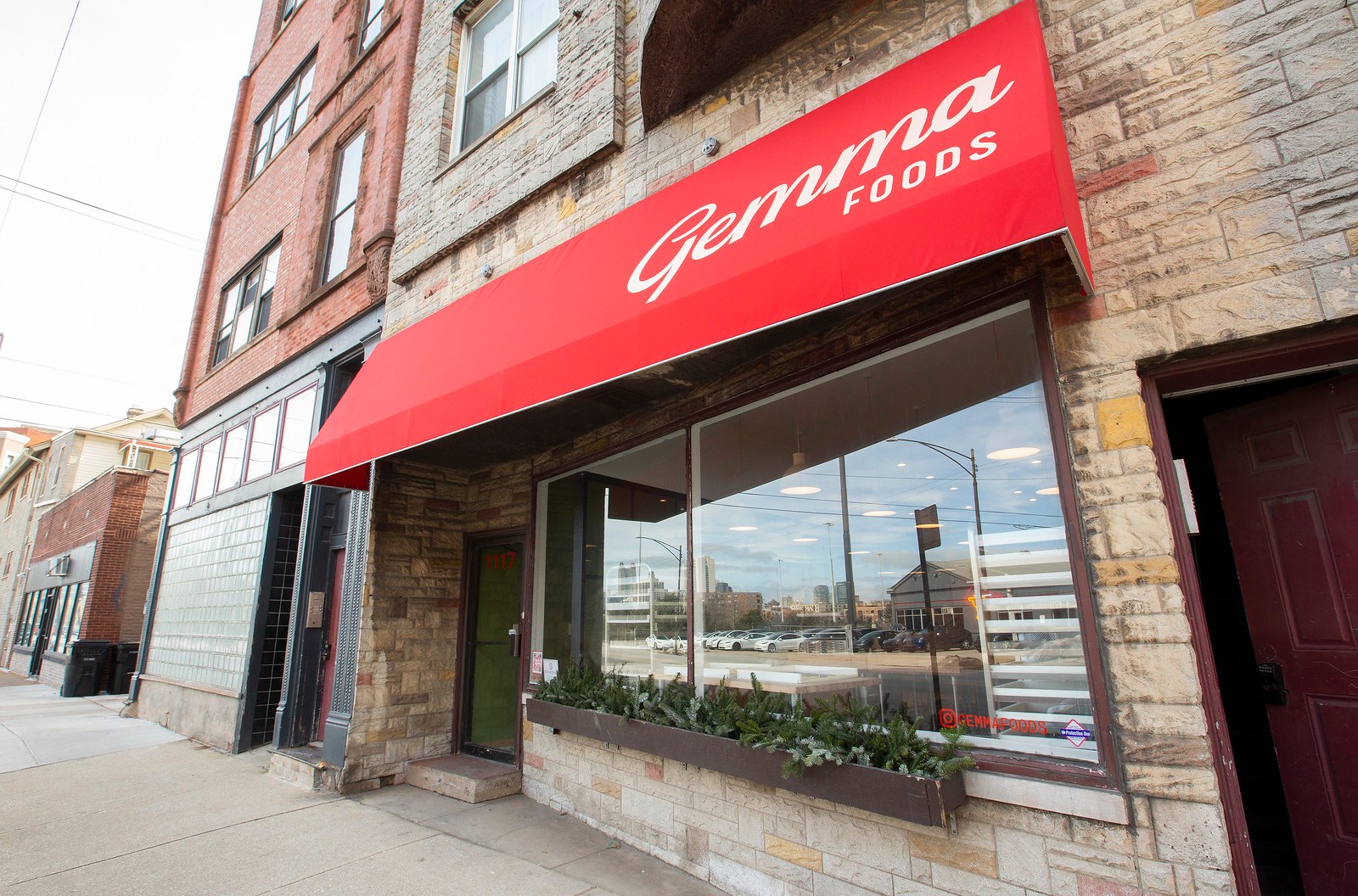 A storefront in with a big front window and a bright red awning.