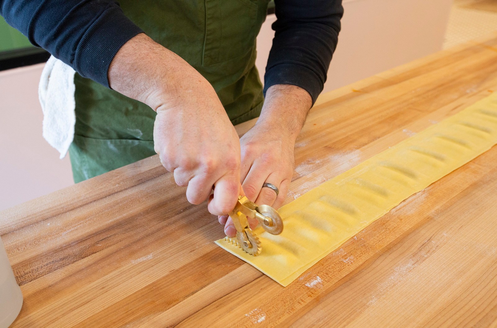 A chef uses a pastry wheel to cut a sheet of pasta into individual ravioli.