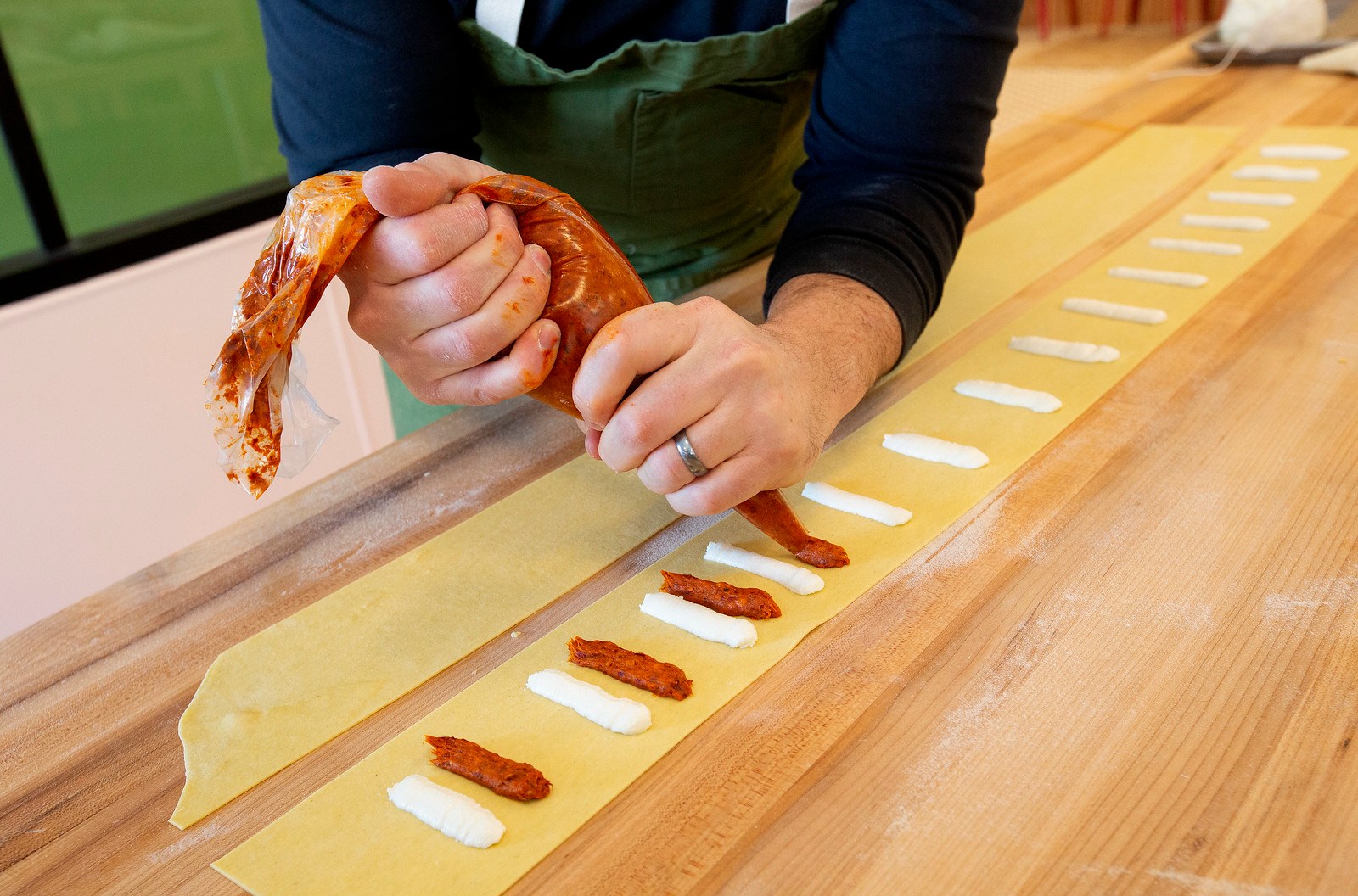 A chef pipes stripes of tomato sauce beside stripes of ricotta cheese on a sheet of pasta.
