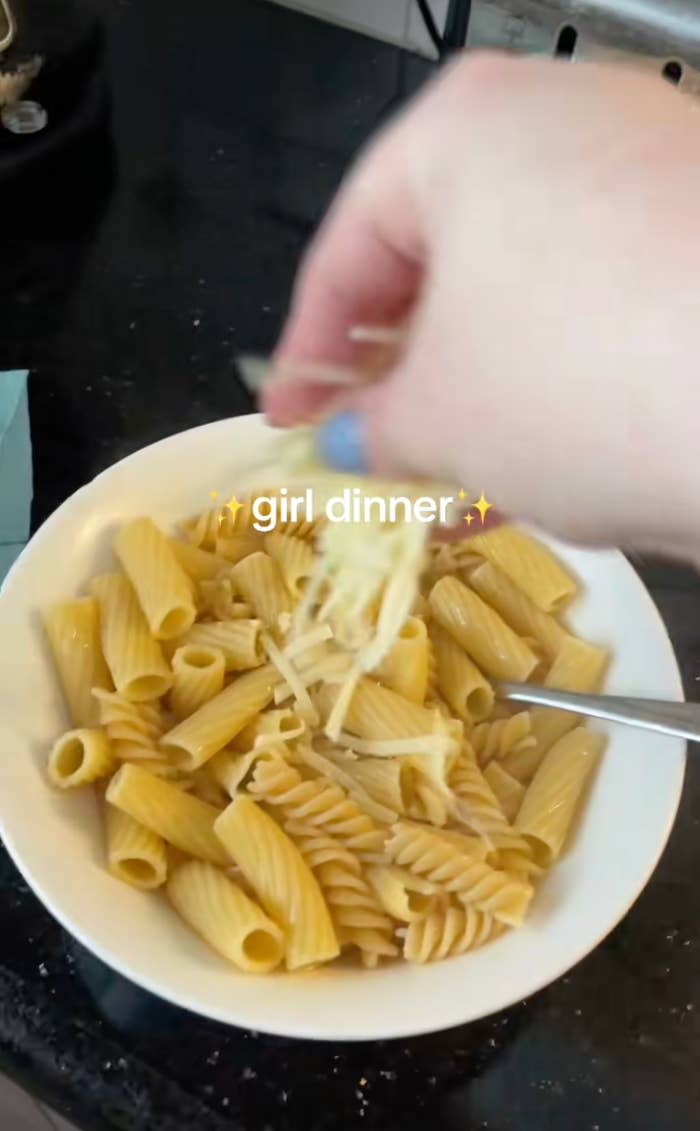 A bowl of mixed pasta shapes being sprinkled with cheese, captioned "girl dinner."