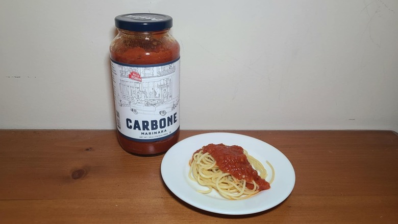 Jar of Carbone pasta sauce with a small white plate of spaghetti topped with sauce