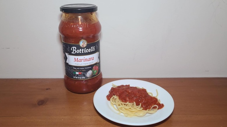 Jar of Botticelli pasta sauce with a small white plate of spaghetti topped with sauce