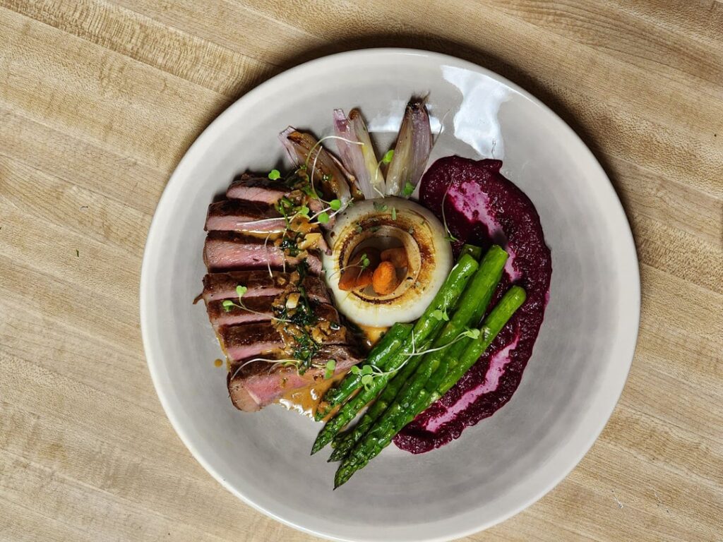 Steak au Pouivre with roasted onions, camelized shallots, glazed carrots, sautéed asparagus, beet puree, and micro-greens