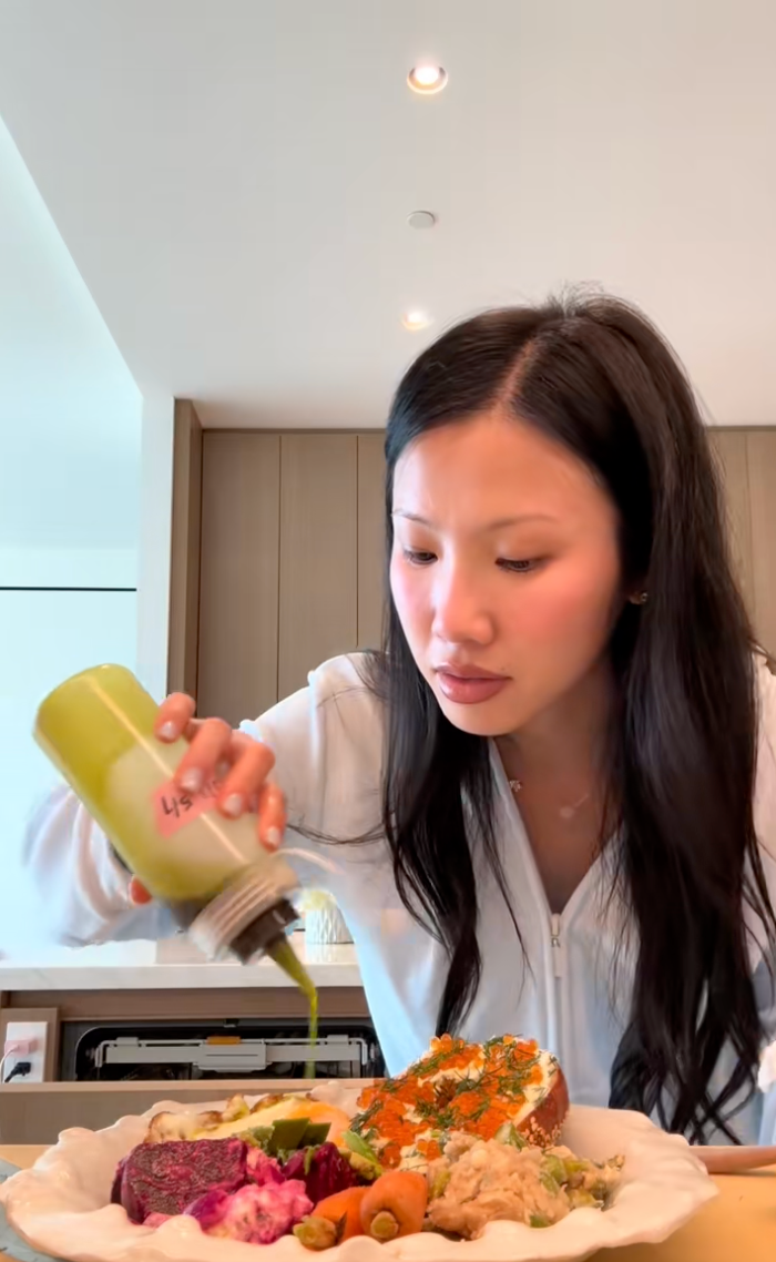 Person pouring green sauce over a diverse salad on a plate in a modern kitchen setting