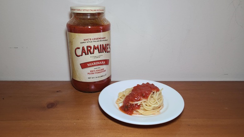 Jar of Carmine's pasta sauce with a small white plate of spaghetti topped with sauce