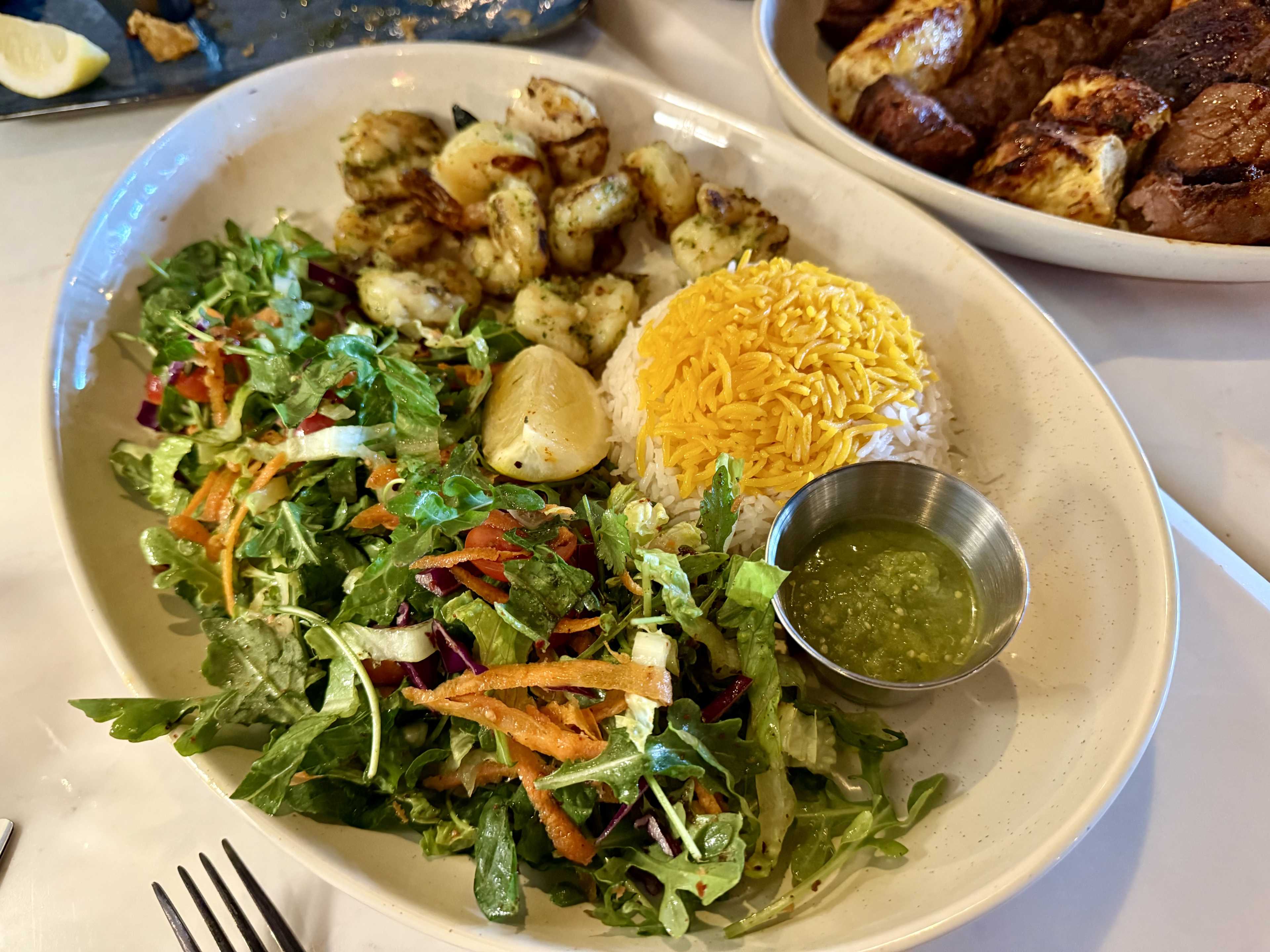 A plate of grilled shrimp, rice, and a side salad.