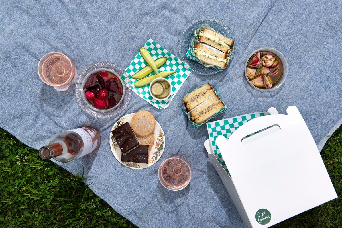 A gray blanket features pickled items, an egg sandwich, and green checkerboard sandwich paper. 