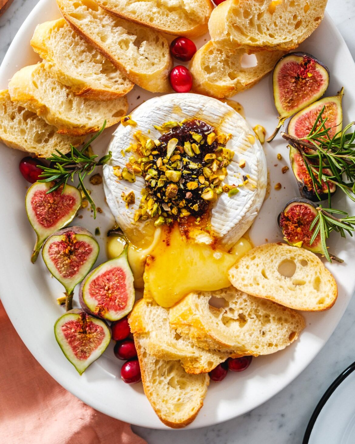 Easy Christmas appetizer spread with baked brie topped with jam, honey and pistachios with crostini and figs