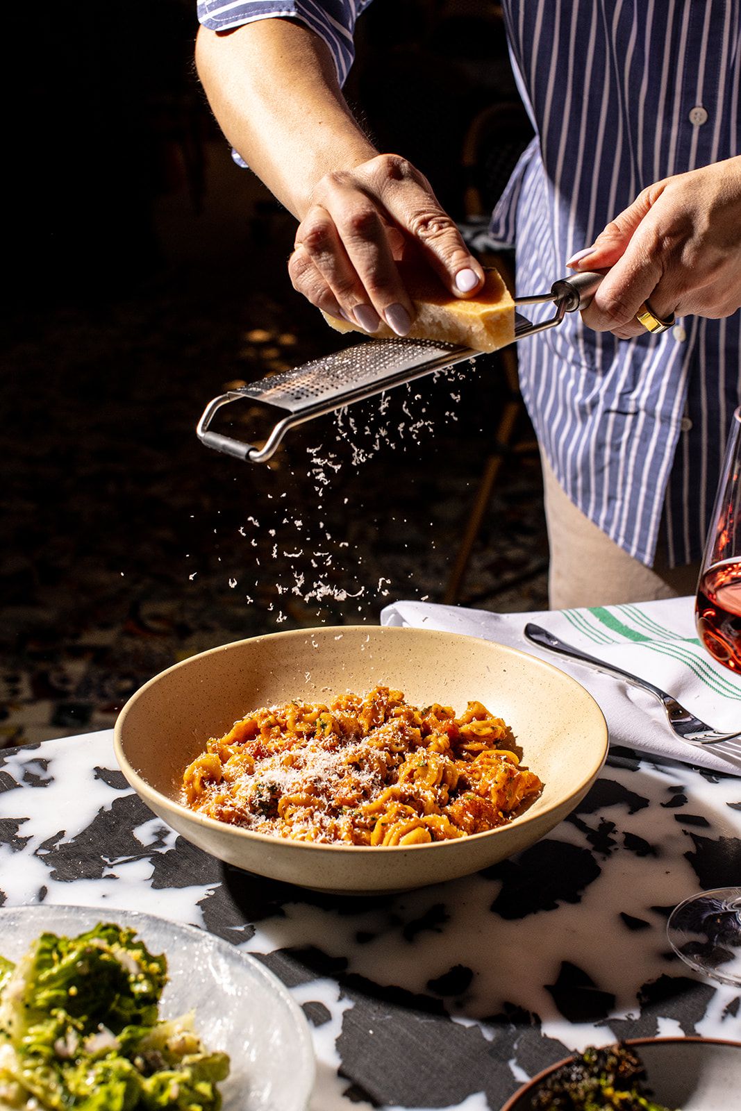 Hand grating Parmesan cheese of a bowl of radiator at Bar Issi