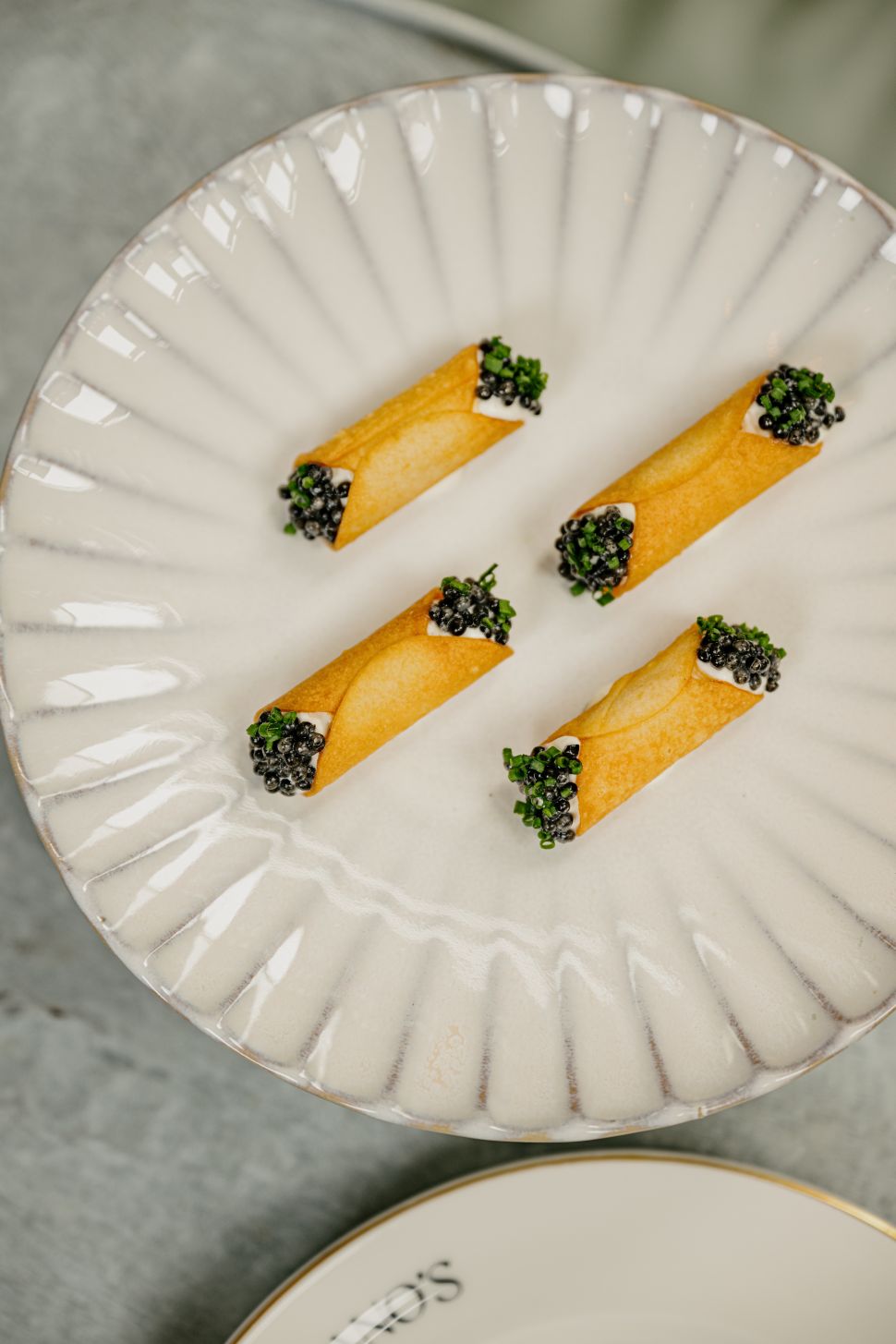 A delicate dish featuring crispy, golden cannoli filled with a creamy mixture and topped with black caviar and fresh herbs, served on a white plate.