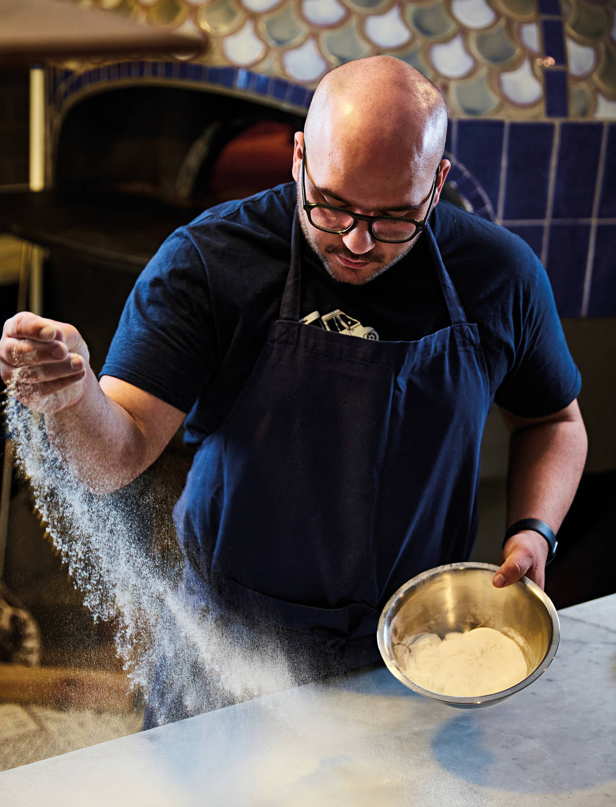 a pizza chef sprinkling his worktop with flour