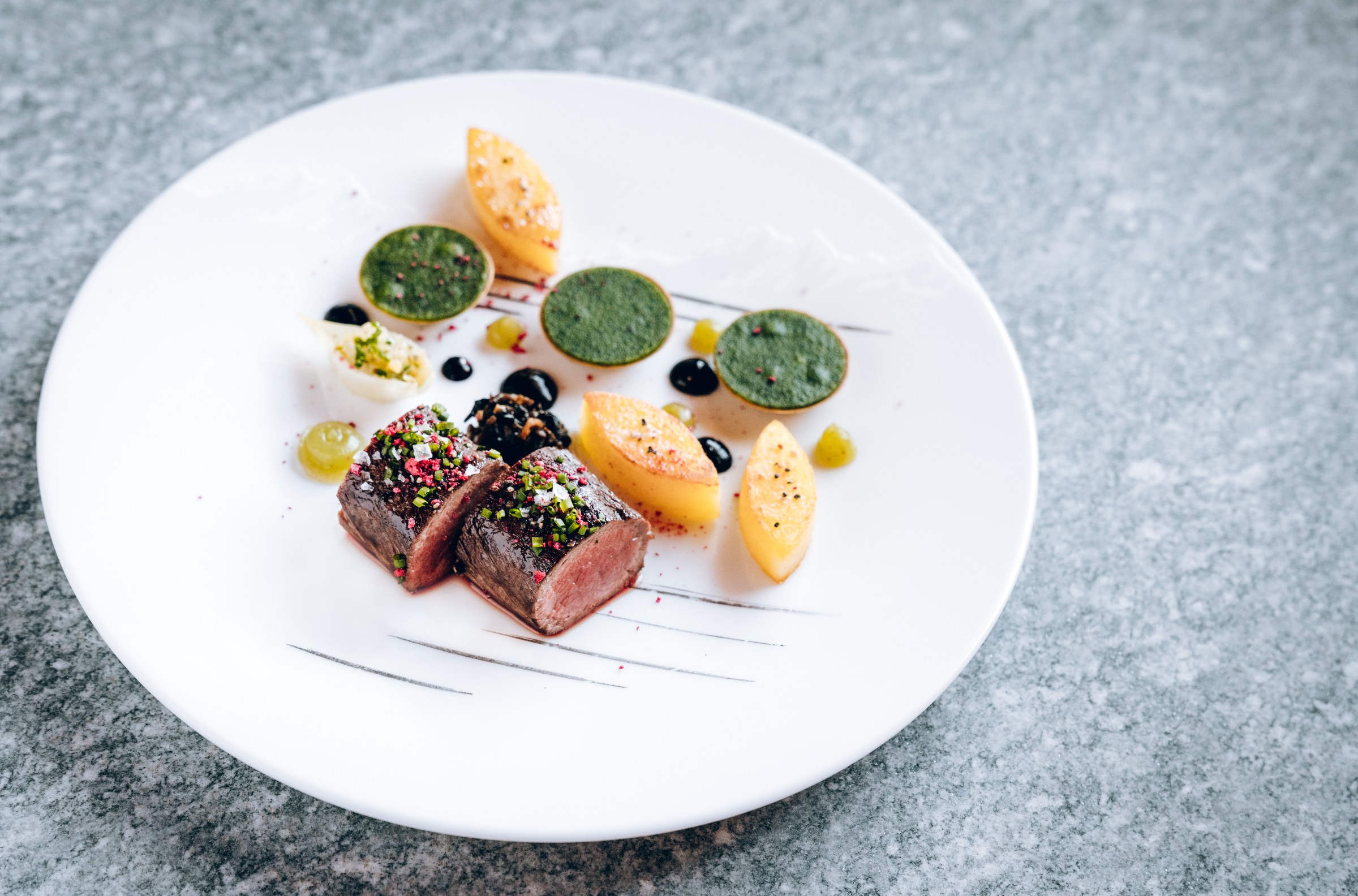 Hunks of rare-cooked meat artfully arranged on a plate beside sides formed into ornate shapes